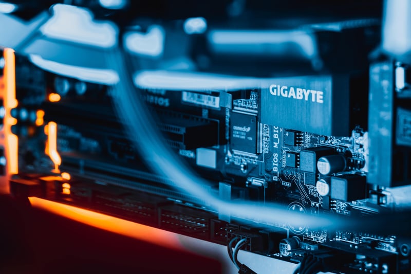 A close-up photograph of a motherboard, lit in blue and orange. 